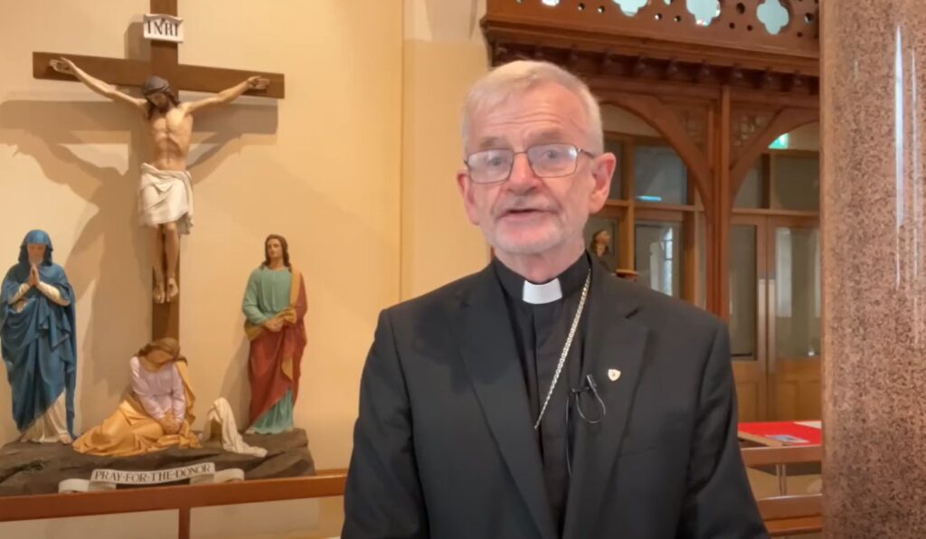 Bishop Alan McGuckian standing in a church with a statue of the crucifixion of Jesus in the background